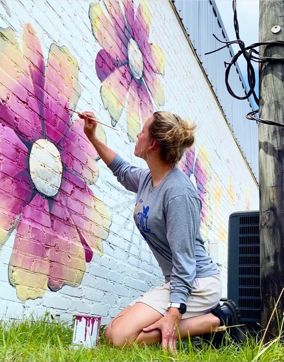 Muralist Christina Donahon adds detail to a mural of Florida wildflowers she’s painting downtown on the Back Home Bakery and Café side wall.