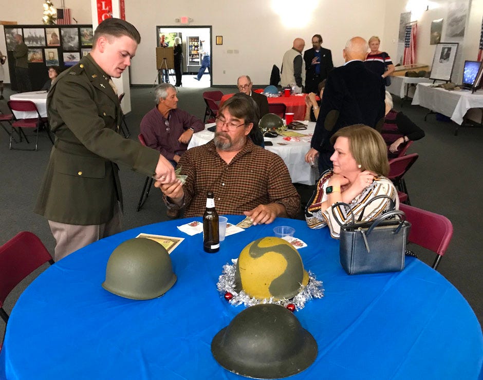 Paul and Kimberly Deichelbor pay Swing into the Season organizer Dako Morfey $100 upon winning an auction for a pair of World War II helmets. The event, held Nov. 27 in Crestview, was a fundraiser for Crestview’s April 22-24 World War II reenactment weekend.