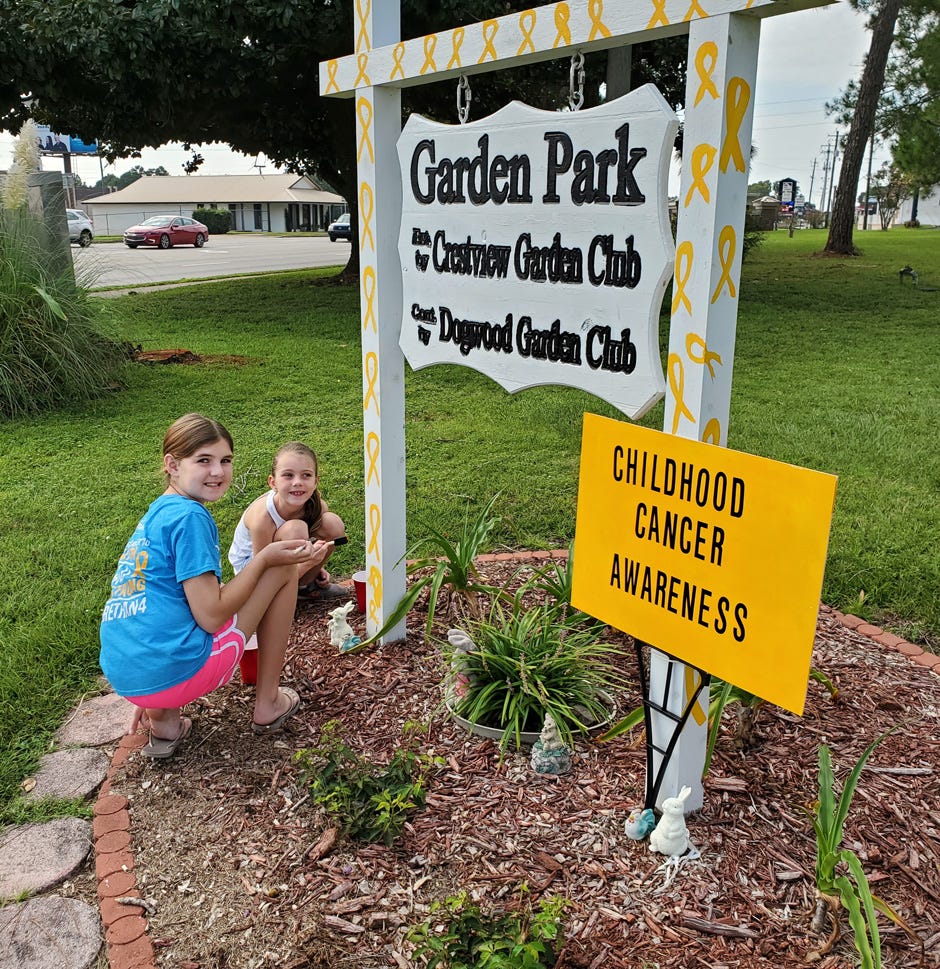 Survivor Katie, left, and her cousin Carys support Childhood Cancer Awareness by placing a sign at Garden Park in Crestview.