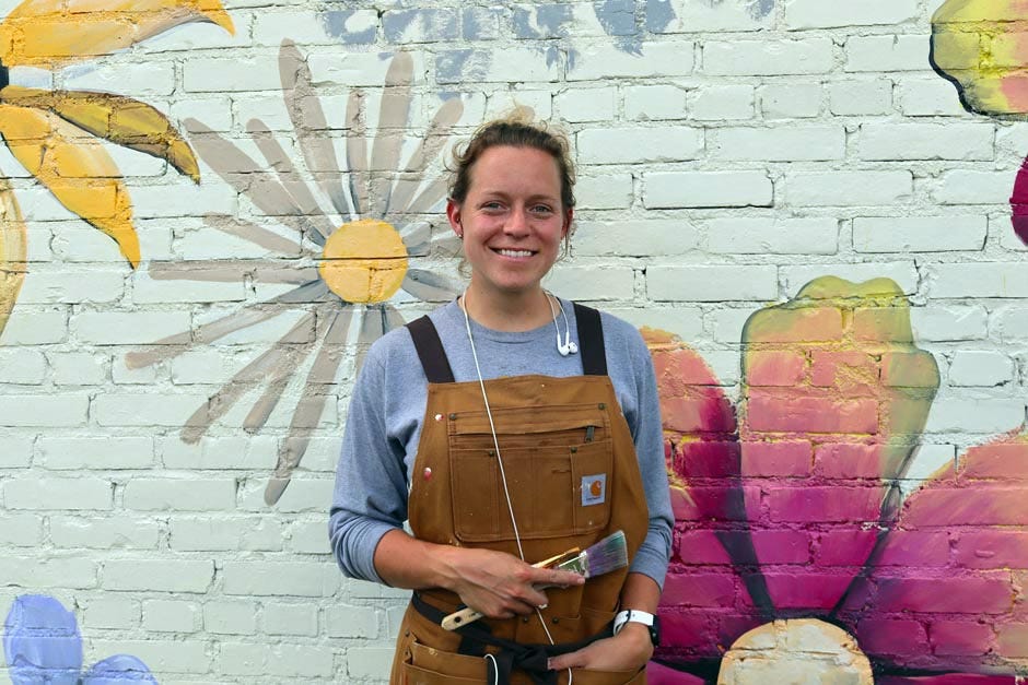 Muralist Christina Donahon stands among the Florida wildflowers that form a mural she’s painting in downtown Crestview.