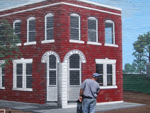 An inmate artist paints details on a depiction of the Bank of Baker, which stood across Baker Block Museum on State Road 189.