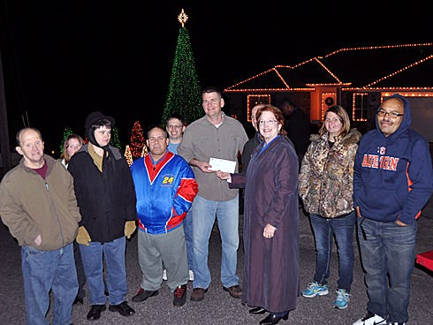 Matthew Neville, center, hands a $320 check to Kim Christopher, director of the Okaloosa and Walton County Special Olympics, while surrounded by Special Olympics athletes on Saturday, the final night of Watts Up Crestview's synchronized light show in the Shoal Lake neighborhood.