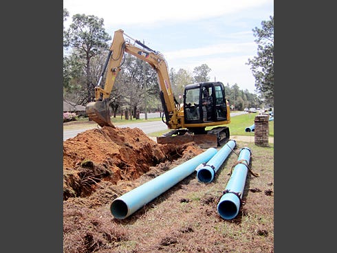 A backhoe operator prepares to bury pipes along Old Bethel Road for a new water distribution system.