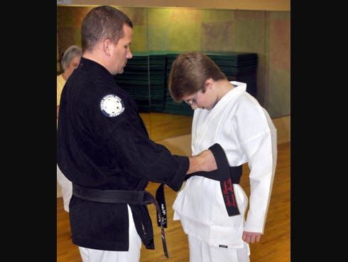 John Lee, lead instructor at Martial Arts Combat Academy in Niceville, assists 14-year-old Harrison Mauldin in wearing an honorary black belt the martial arts school provided on Saturday. Harrison received the belt for his Special Olympics achievement and positive attitude.