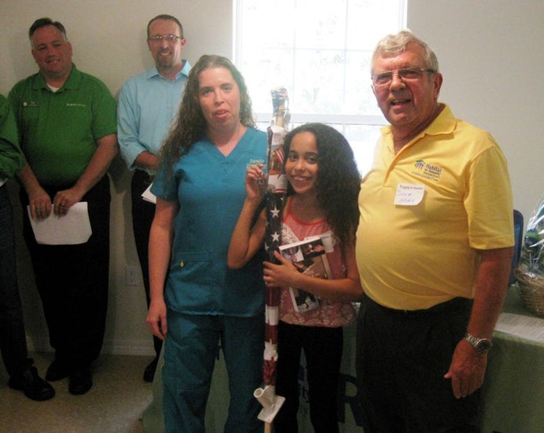 New Habitat for Humanity homeowner Jamie Peoples and her daughter, Ondrea, 11, receive keys to their new house from construction co-manager Dave Hyre as Publix supermarket manager Tim Bryant and the Rev. Jeff Burnett observe. Ondrea holds both the keys and a flag donated by the Republican Women of Okaloosa Federated. (BRIAN HUGHES | News Bulletin)