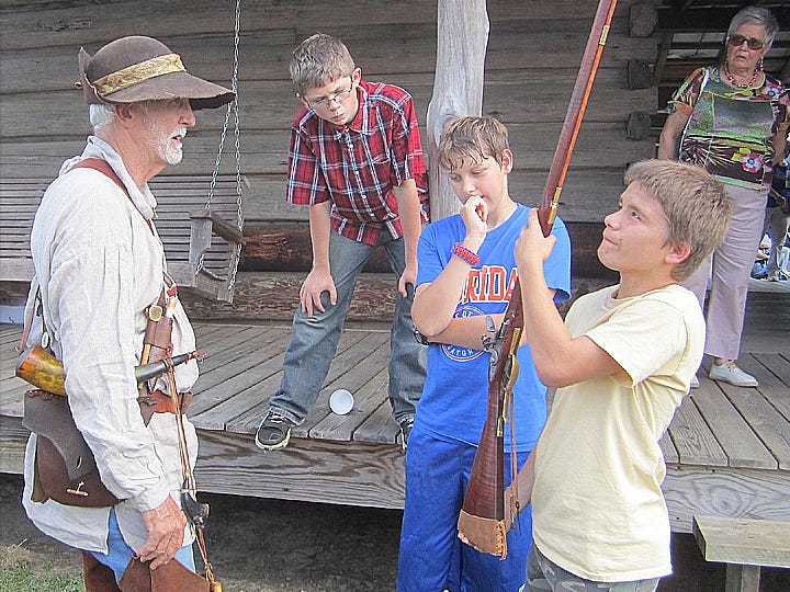 Baker School students Hunter Polhlopek and Wyatt Shumway observe as their friend Danny Turner weighs the heft of colonial-era Florida re-enactor John Butler’s frontier muzzle-loaded rifle at the 2012 Baker Heritage Festival.