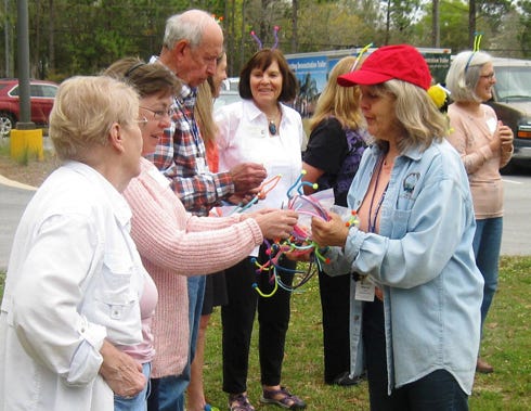 To illustrate how pollinators spread pollen, Okaloosa County Master Gardener Stacy Taylor, in red hat, organizes a game of “Buzzy Bees” with other Master Gardeners.