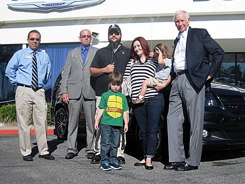 Navy veteran Ken Greathouse, center, and his family — including wife Victoria and sons Logan and Anthony — are flanked by Lee Chrysler Dodge Jeep sales manager Jay Frederickson and salesman Robert Fickett, left, and dealership owner Bob Lee, right, as they take possession of their new Caravan minivan.