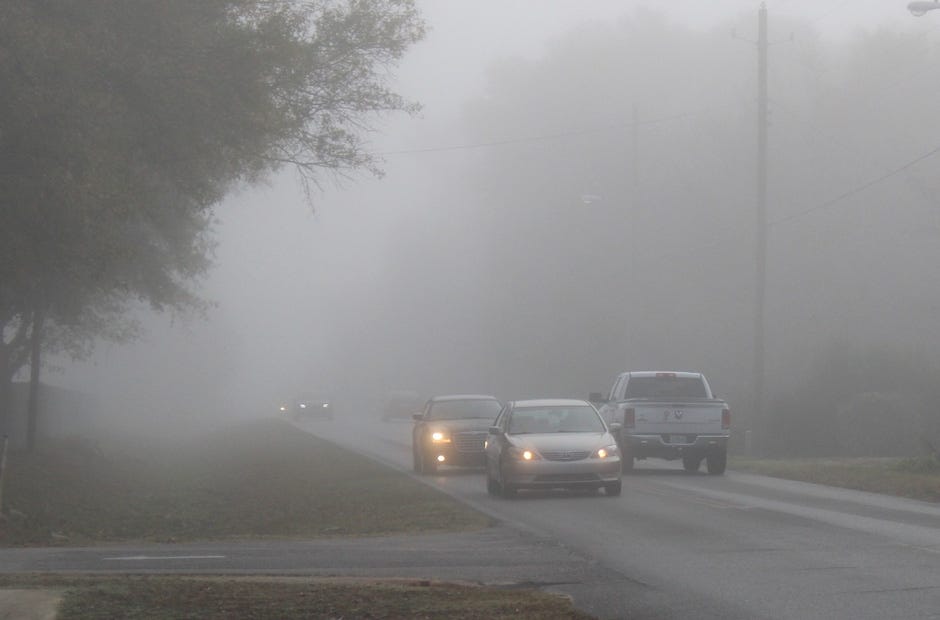 Vehicles drive in a recent dense morning fog on a Crestview street. Note how the car without its lights on blends in unsafely with the fog, while vehicles with headlights are more visible. [Brian Hughes | Crestview Police Department]