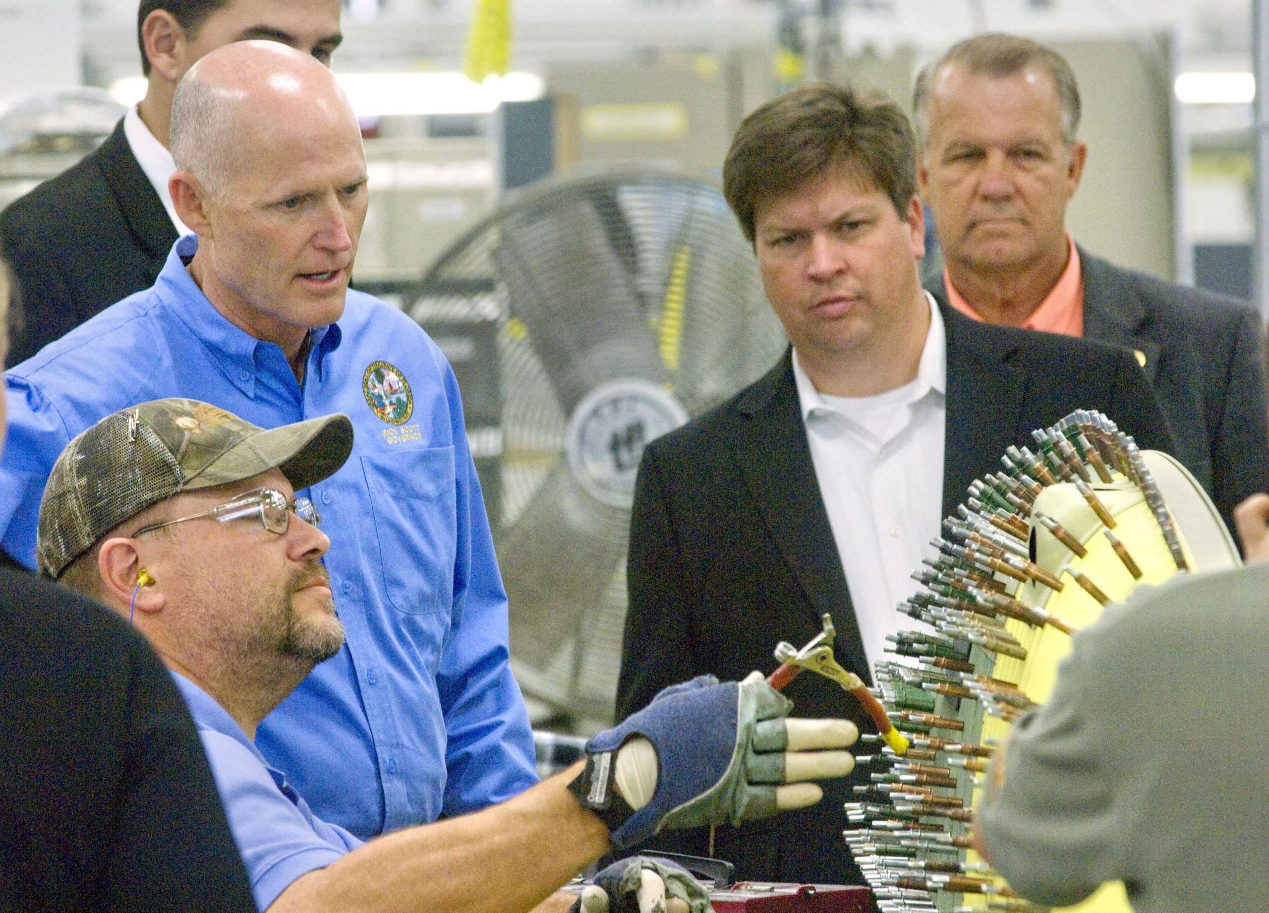 Florida Gov. Rick Scott, blue shirt, talks with Scott Motteler, seated, about an aircaft part he was working on at L-3 Crestview Aerospace in 2012. [FILE PHOTO/DAILY NEWS]