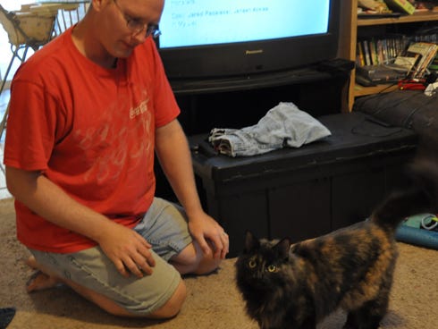 Chris Gearhart kneels beside his cat, Syn, at his Crestview home. Syn received a broken jaw, broken floating ribs, a concussion and injuries to the heart and lungs in a Sept. 28 fight.