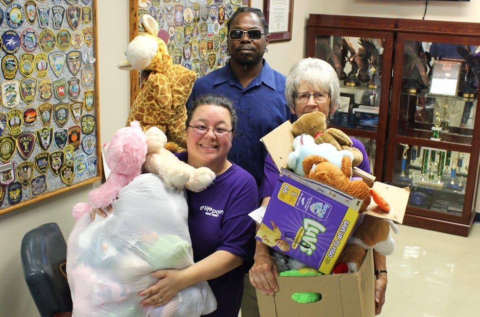 Georgia Barlow and Julie Doane of Lifepoint Church stagger under a mound of stuffed animals their Kids Mart shop donated to the Crestview Police Department. An unidentified resident who happened to be visiting the CPD offered his services to help the ladies bring the toys into the lobby. [Brian Hughes | Crestview Police Department]