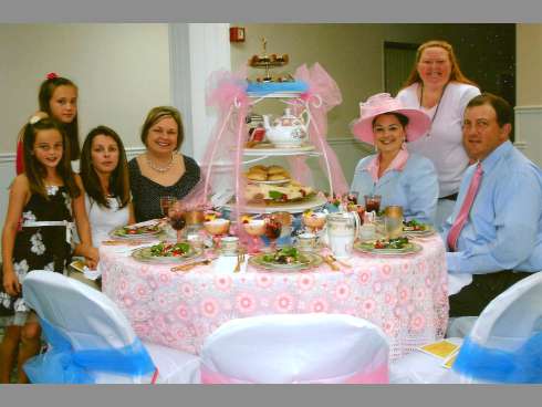 Crestview City Councilwoman Robyn Helt, seated second from right, dons a hat for the 2012 Kentucky Derby-themed tea, coordinating her attire and her husband Scott’s with her soft pink and blue tablescape.