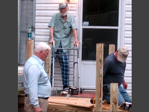 Mickey Givens, standing on the porch, watches as volunteers construct a ramp at his Laurel Hill home.