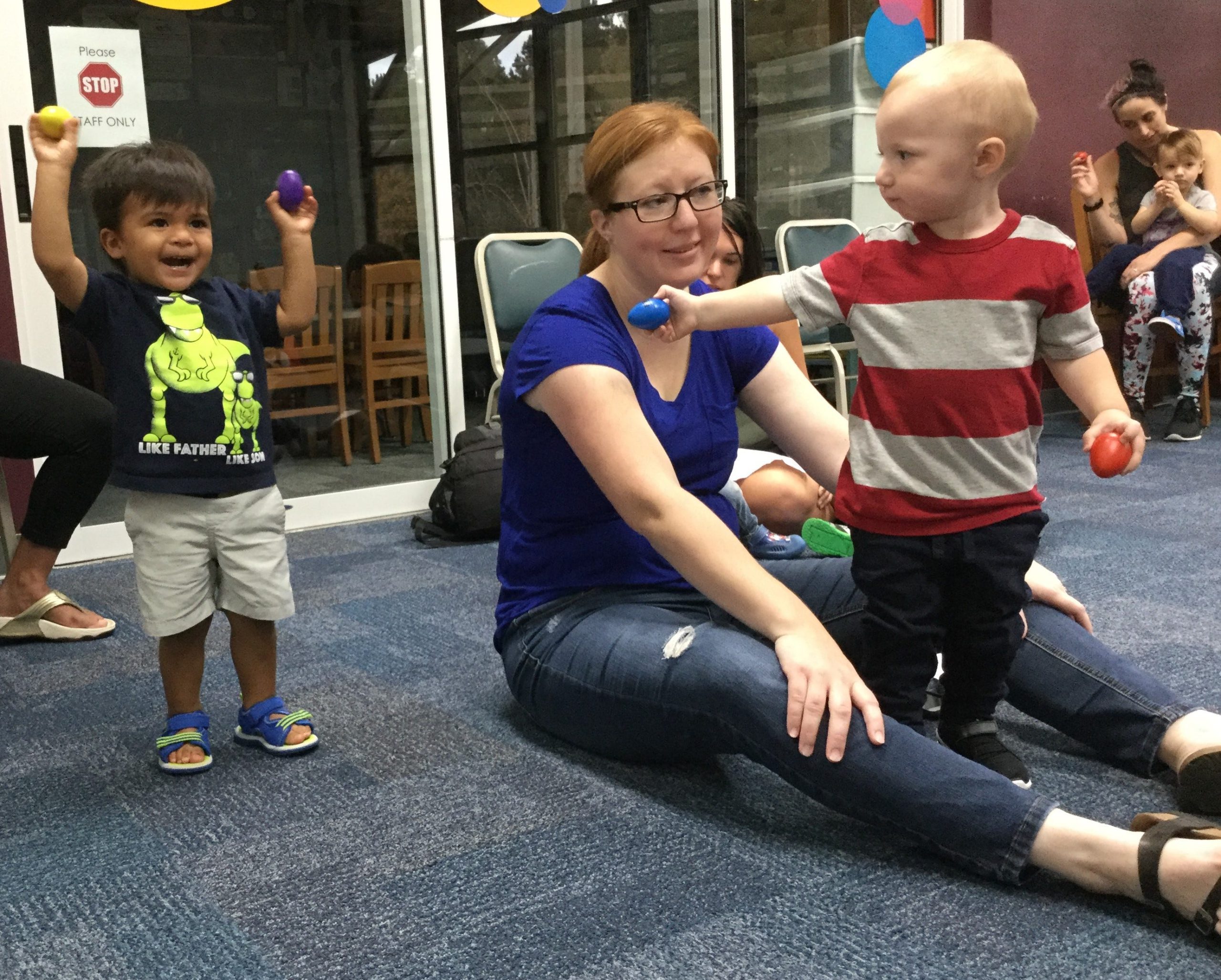 Cesar Estrada II (age 1) shakes his eggs high during the Dec. 1 Ages 0-2 Library Class. Grant Reeves (also age 1) offers, “Want to try to blue?” making mom Kristen Reeves smile. All are Crestview residents. [Special to the News Bulletin]