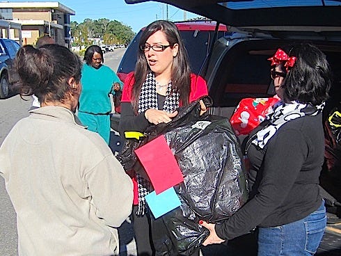 Courtney Baker, center, and Jennifer Garraty-Hargett, right, of Catholic Charities of Northwest Florida give a sack of toys to a mother of young children Wednesday morning.