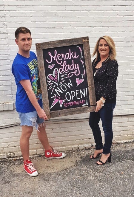 Dale Riley III and Shelly Brace hold a sign created Dec. 20 for their women's boutique, Meraki Lady, at 265 Main St. N. in Crestview. [MERAKI LADY | SPECIAL TO THE NEWS BULLETIN]
