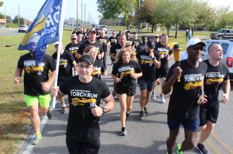 Crestview Police Department Cadet Officer Justin Wallen carried the Law Enforcement Torch Run flag part of the way down Industrial Drive March 28 in Crestview. CPD Critical Systems Manager Kathy Duke, center, also carried it. [BRIAN HUGHES | CPD]
