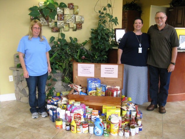 Sharing and Caring President Robin Marston, hope chest winner Wendy Farmer and the chest’s craftsman, Larry Hunter, flank food bank donations provided by Dr. Jennifer Wayer’s patients.