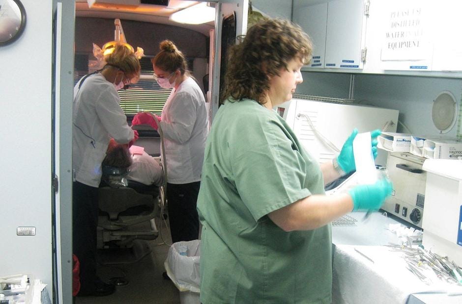 As Susan Welch and dental assistant Melissa Randall extract a tooth, Florida Baptist Convention mobile dental unit coordinator Crystal Andrews sterilizes equipment during the clinic's stop May 6, 2016 in Baker. [FILE PHOTO | NEWS BULLETIN]