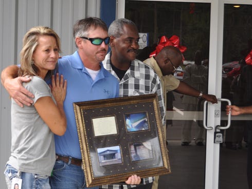 Connie and Heath Oglesby stand next to the Rev. Darrell Coleman, of Praise, Power and Compassion Ministries, during a ribbon cutting ceremony for the church’s new building at 2188 James Lee Blvd. Heath is holding a gift from the church that commemorates their son, Wyatt.