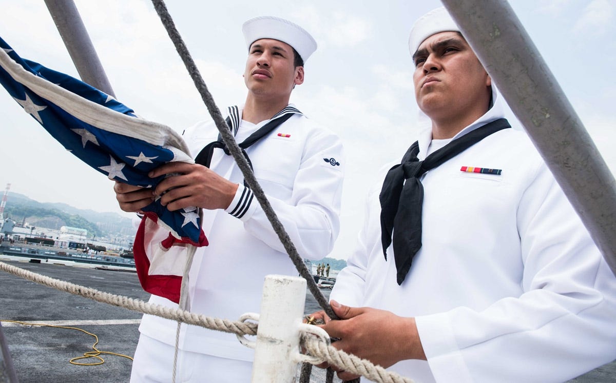 Airman Paris Alexander, left, of Crestview, and Aviation Boatswain's Mate (Handling) Airman Terrence Garcia, from El Paso, Texas, stand by to hoist the national ensign on the flight deck of the Navy's forward-deployed aircraft carrier, USS Ronald Reagan (CVN 76) as it pulls into Commander, Fleet Activities Yokosuka after a patrol in Japan. Ronald Reagan, the flagship of Carrier Strike Group 5, provides a combat-ready force that protects and defends the collective maritime interests of its allies and partners in the Indo-Pacific region. [KENNETH ABBATE | U.S. NAVY]