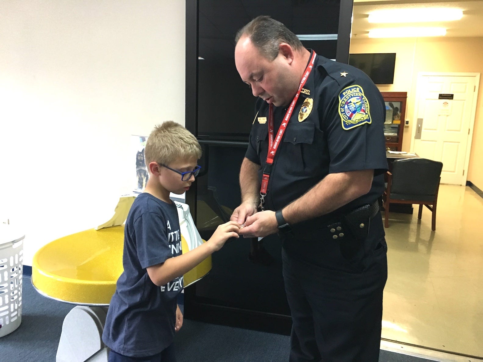 Crestview Police Deputy Chief Jamie Grant presents the agency’s “policeboy,” Jae Williams, with an official CPD lapel pin and challenge coin as mementoes of his many visits bearing gifts for Crestview Police officers. [PHOTO BY BRIAN HUGHES | CRESTVIEW POLICE DEPARTMENT]
