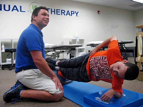 “I hate these,” Drew Barefield said of side plank exercises as his physical therapist, Dan Foradori, watched the clock. Drew had to hold the position for 30 seconds before switching sides.