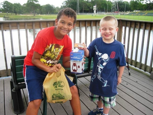 Fishing campers Matthew Mitchell, 9, and Gavin Raabe, 5, display the contents of goodie bags they received from Bass Pro Shops. An LED lantern and fishing lures were among items the Destin store donated for Crestview fishing camp participants.