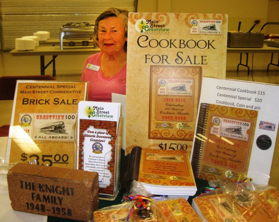 Main Street Crestview Association manager Patti Gonzo displays Crestview Centennial mementoes available at Saturday's birthday celebration and at City Hall. Included are a commemorative cookbook, specially minted coins, a logo pin and dedicated Main Street sidewalk bricks.