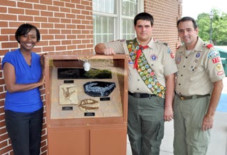 Patrice Williams, the Robert L.F. Sikes Education Center’s director, Boy Scout Brandon Woods and Troop 773 leader Kelly Carrico surround Woods’ Eagle Scout project, a dinosaur fossil replica display, on Friday at the Crestview campus.