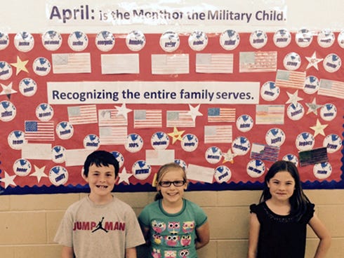 Walker Elementary School students — from left, Brayden Jones, Kiera Parry and Kaylee Mercer — stand in front of a board recognizing military-connected students as they observe Month of the Military Child.