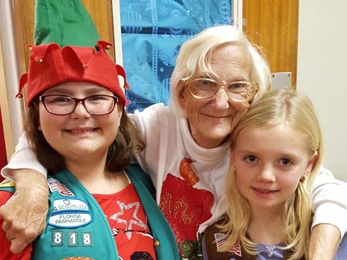 Isabelle Lindstrom, from Troop 818, left, and Skylar Calhoun, of Crestview Troop 676, stand with Crestview Manor resident Marjorie Willsey Dec. 15 at the assisted living facility.