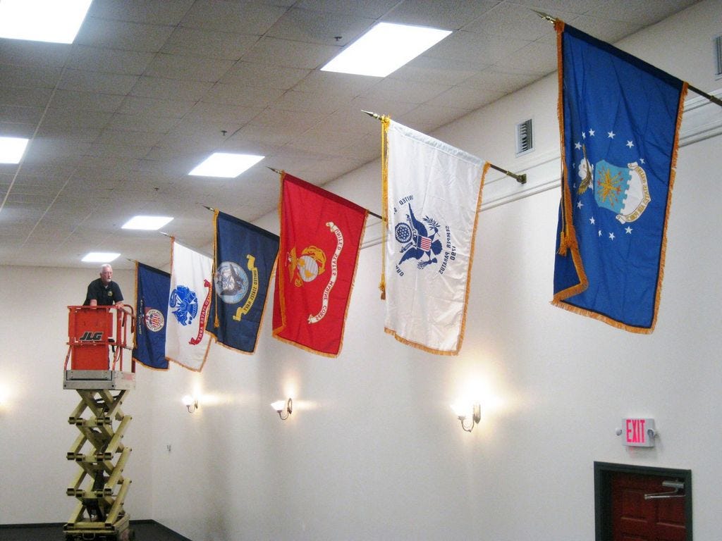 Crestview Public Works assistant director Chuck Powell maneuvers a scissors lift into position as he makes final adjustments to the display of U.S. service branch flags in Warriors Hall. The display includes military service flags displayed in order of the branch's establishment.