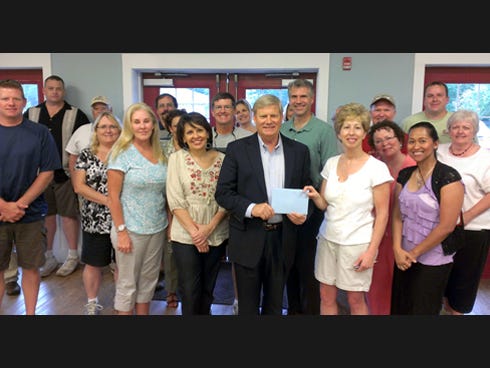 Ken Hair, Children in Crisis president, center, receives a signed card and $210 donation from Sharon Pedersen and the JDAM International team during a recent Wingman Day at Children in Crisis.