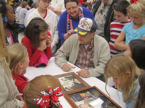 Surrounded by interested Laurel Hill School students, World War II veteran James Cook describes his wartime experiences during the school’s Veterans Day Celebration.