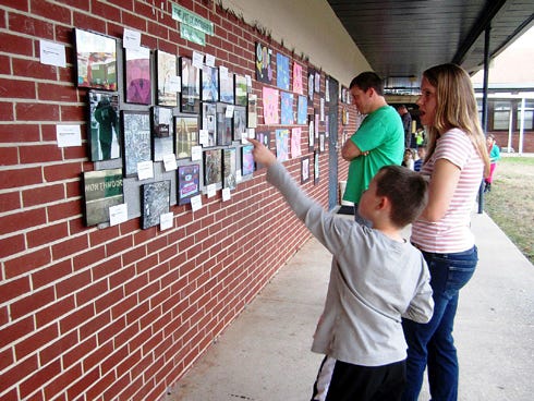 Northwood second-grader Brycen Clouse points out his photography to his parents Kelly and Mark Clouse during the school's ArtWalk exhibit.