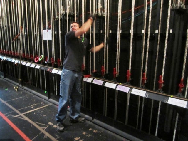 Crestview High School alumnus Josh Long — with green tape on his shoulder signifying he's part of the carpentry crew — controls the ropes to lower and raise drapery and equipment pipes at the Mattie Kelly Arts Center.