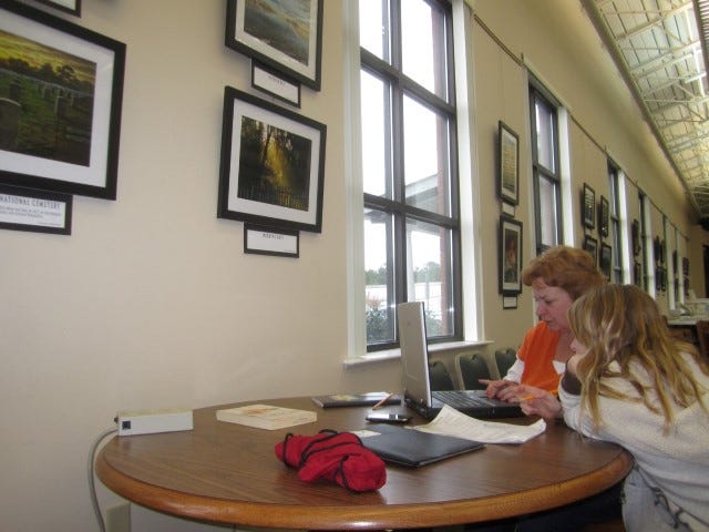 Walker Elementary School student Grace Slentz studies at the Crestview Public Library with her tutor, Robyn Jackson, beneath photos exhibited by the Crestview Photography Club.