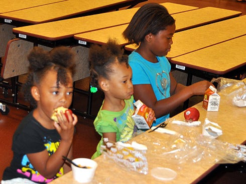 Takayah Johnson, 6, and her sisters, Taylin, 3, and Takyra, 9,enjoy a free lunch on Wednesday at Riverside Elementary School.