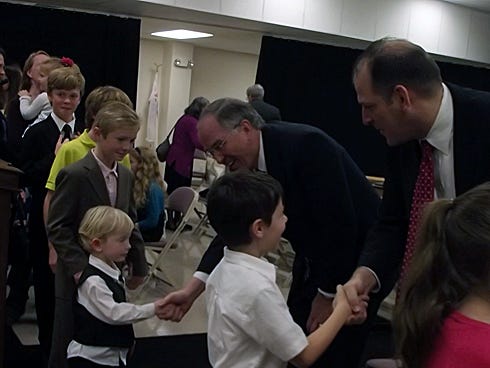 Elder Neil Anderson, center left, and President Mike Roberts of Crestview shake hands with children attending a meeting of Northwest Florida congregations Jan. 18 at the Crestview Community Center.