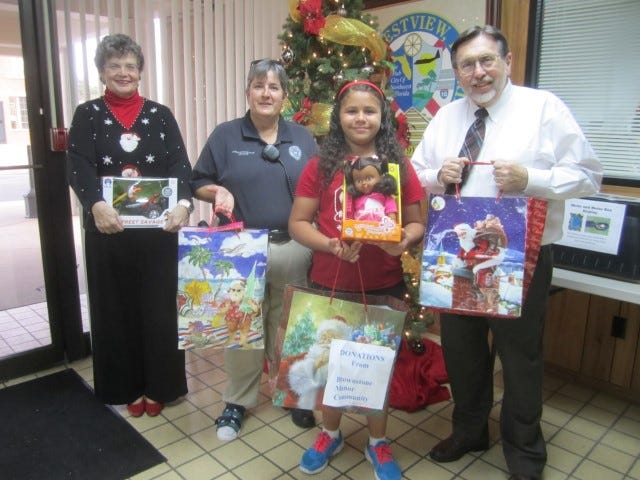 City Clerk Betsy Roy, Crestview community policing officer Wanda Hulion and Mayor David Cadle accept 10-year-old Justice Livingston's toy collections for the Cops for Kids program.